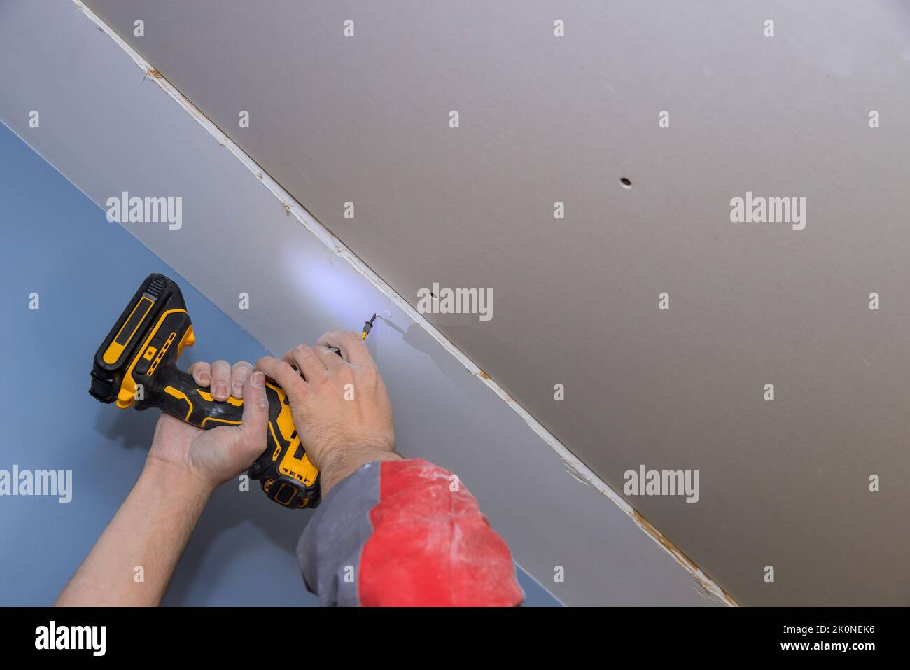 Screwing drywall to the ceiling with worker using screwdriver Stock Photo