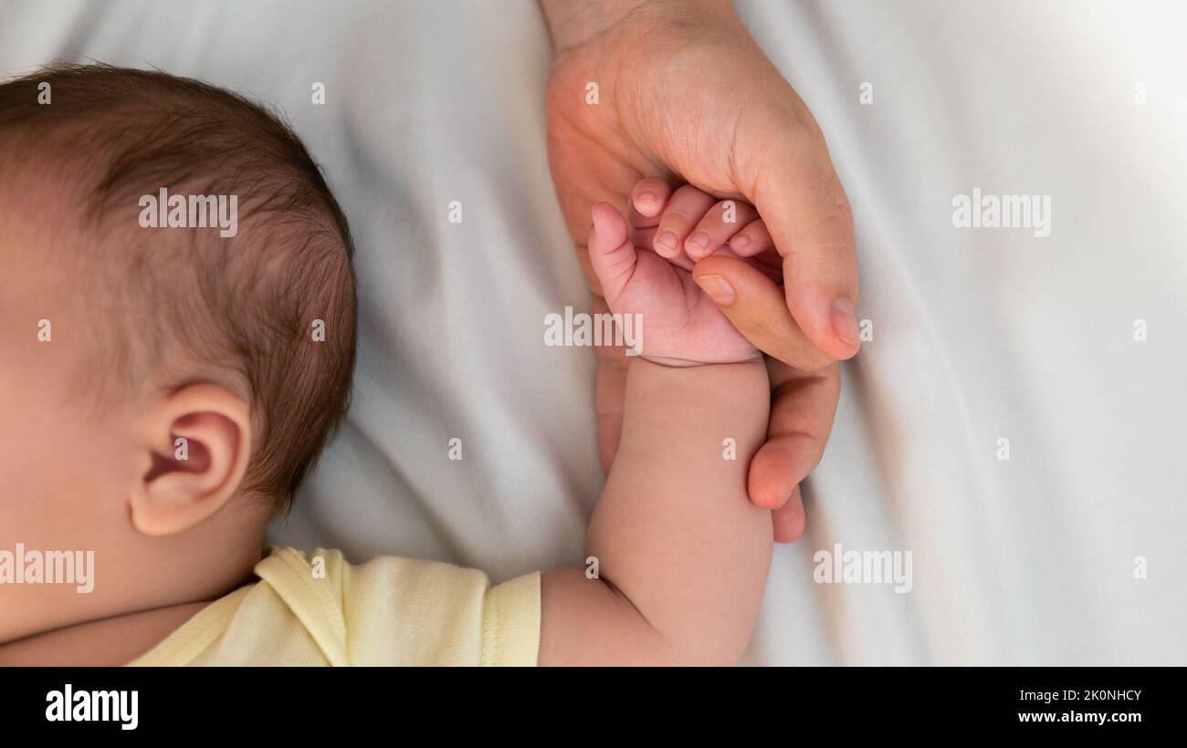 Close up mother holding hands newborn boy in a room with a lot of sunlight. Baby sleeping on the mother's bed. Health care, love and relationship conc Stock Photo