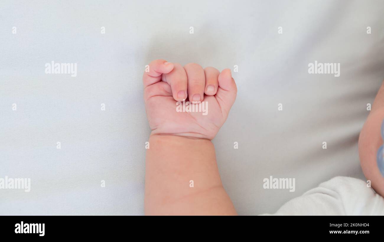 Close up of newborn boy hand on white sheet background. Baby sleeping on the bed. A beautiful conceptual image of childhood. Family and home concept w Stock Photo