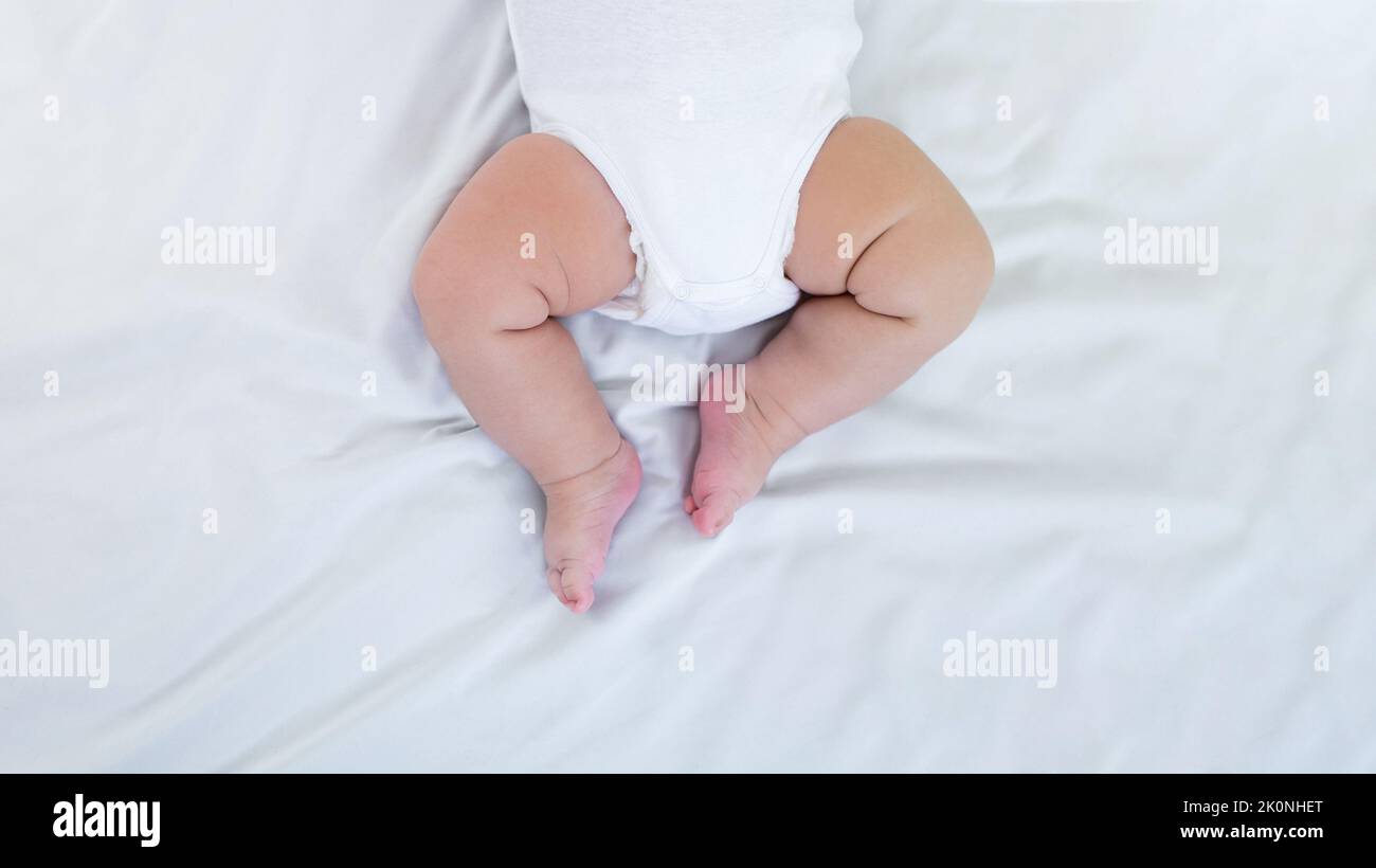 Chubby legs of little baby on white sheet background with day light. Cute newborn age of 3 months. Boy sleeping on the mother's bed. Family maternity Stock Photo