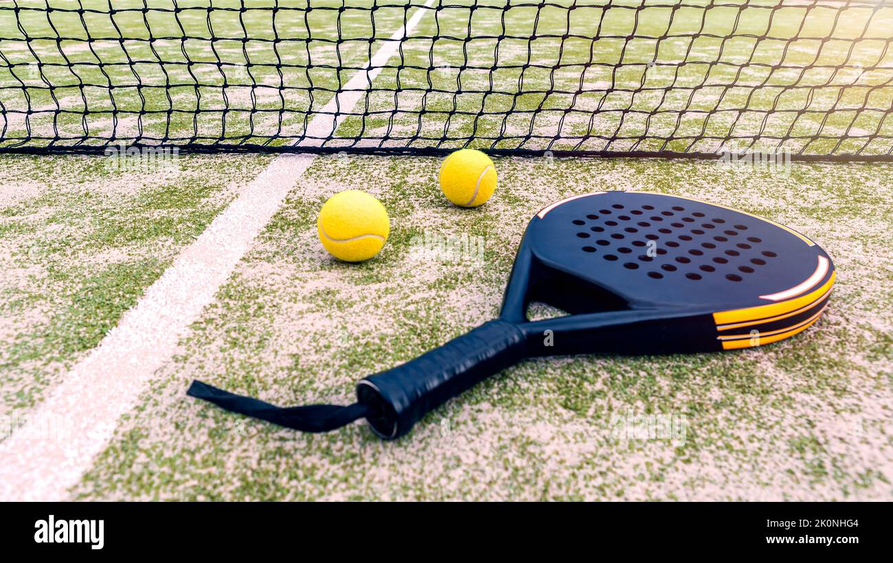 Padel racket and yellow ball behind net on a green court grass turf outdoors. Paddle is a racquet game. Professional sport concept with space for text Stock Photo
