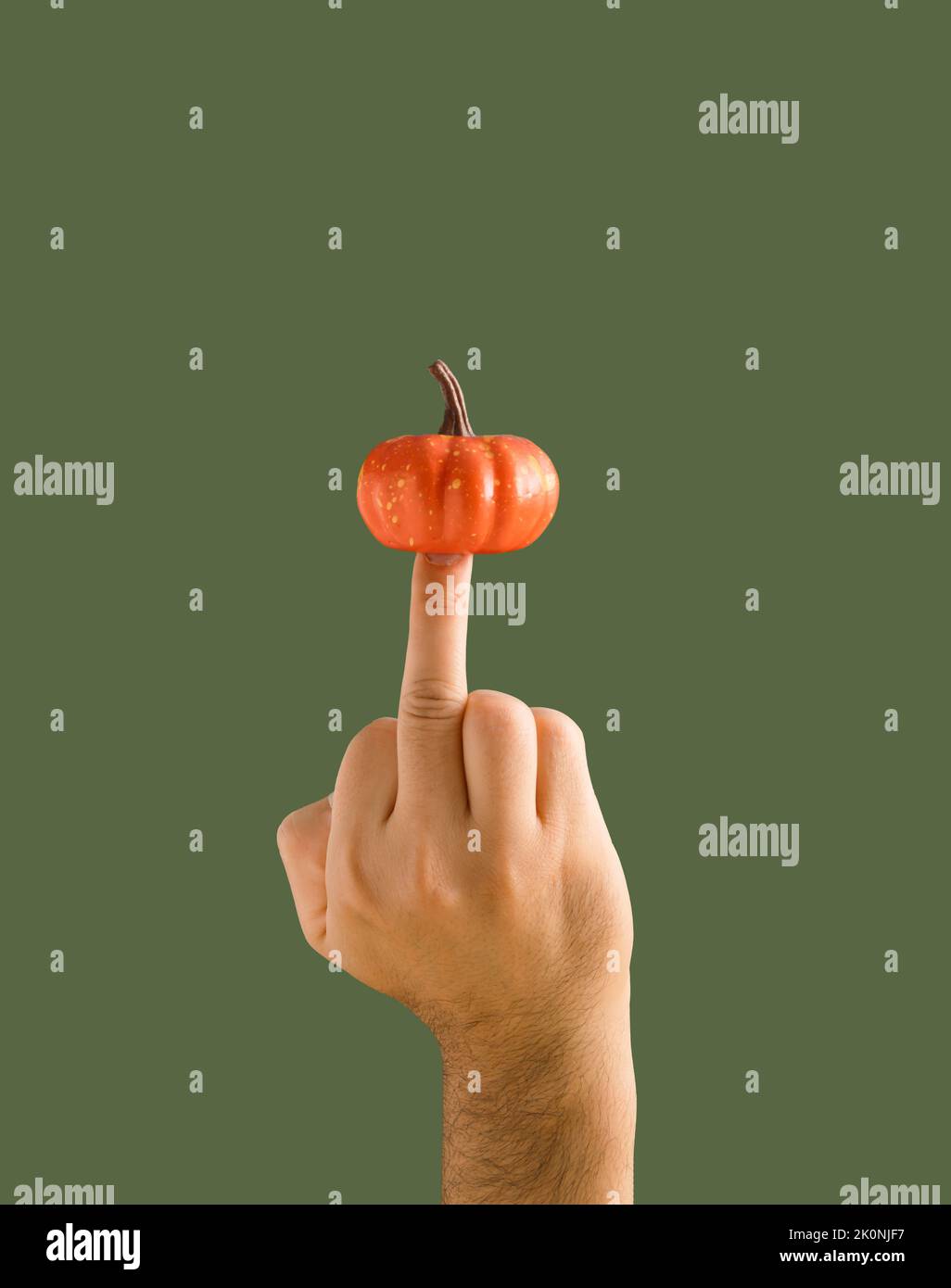 Hand shows aggresive gesture with the middle finger and pumpkin on dark green background. Autumn colors. Seasonal background. Stock Photo