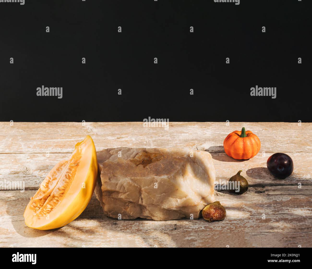 Retro style composition made of melon fruit, figs, pumpkin and rock on old wooden table. Product podium, suitable for product display. Dark background Stock Photo