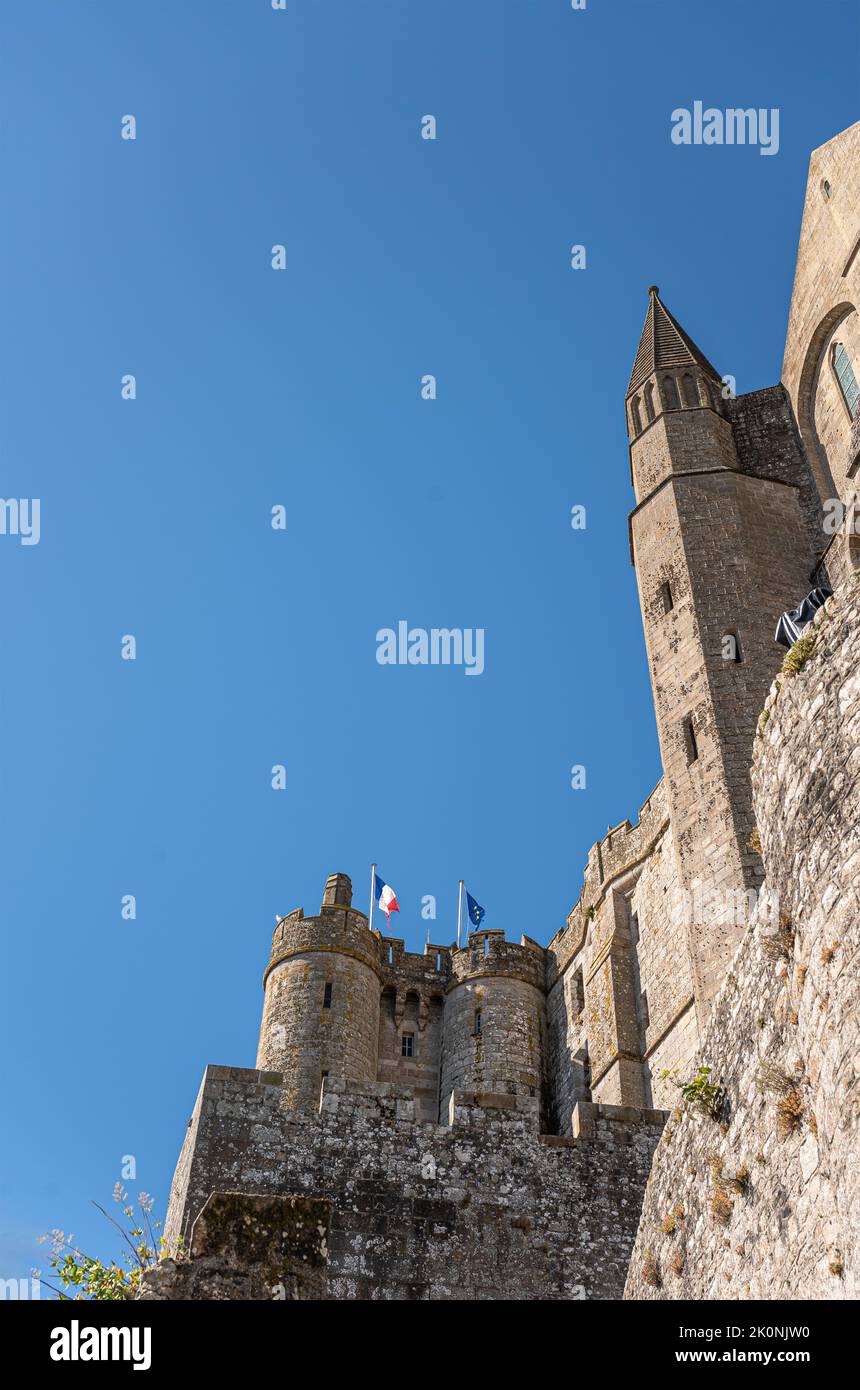 Mont St. Michel, Normandy, France - July 8, 2022: Brown stone castle and church walls detail featuring French and European flag on top against blue sk Stock Photo