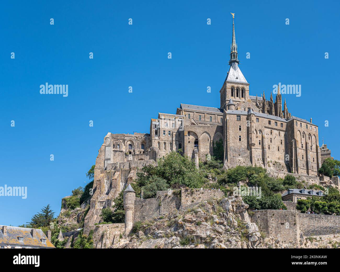 Mont St. Michel, Normandy, France - July 8, 2022: Entire gray stone church building with tower, spire, and St. Michael statue on top, stands on its ro Stock Photo