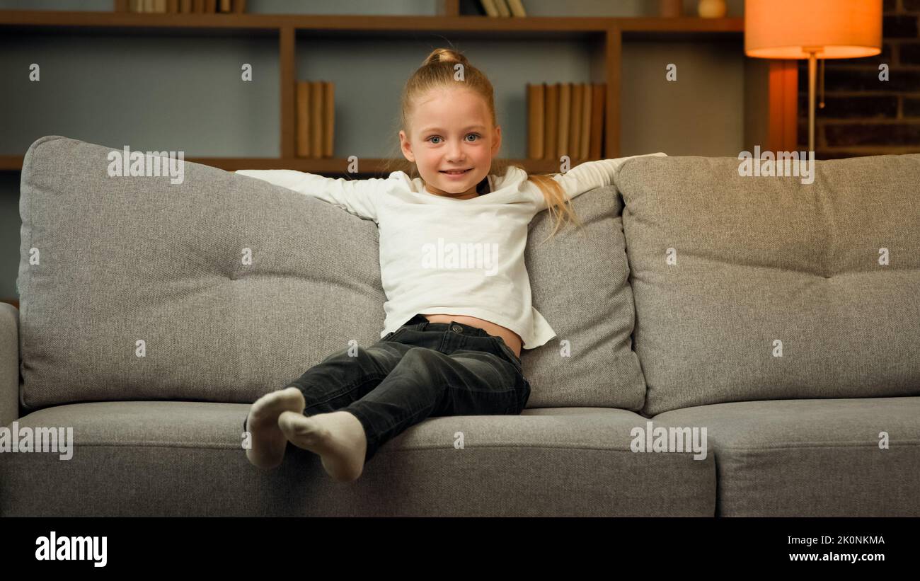 Small blonde school toddler child active kid falling down on comfortable sofa cozy couch for daytime break relaxation time little girl enjoying Stock Photo