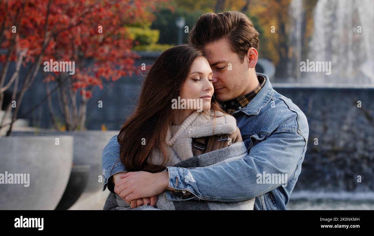 Caucasian couple lovers partners stand background of city fountain pressed closely to cheeks together spend time in autumn park on date embrace feel Stock Photo
