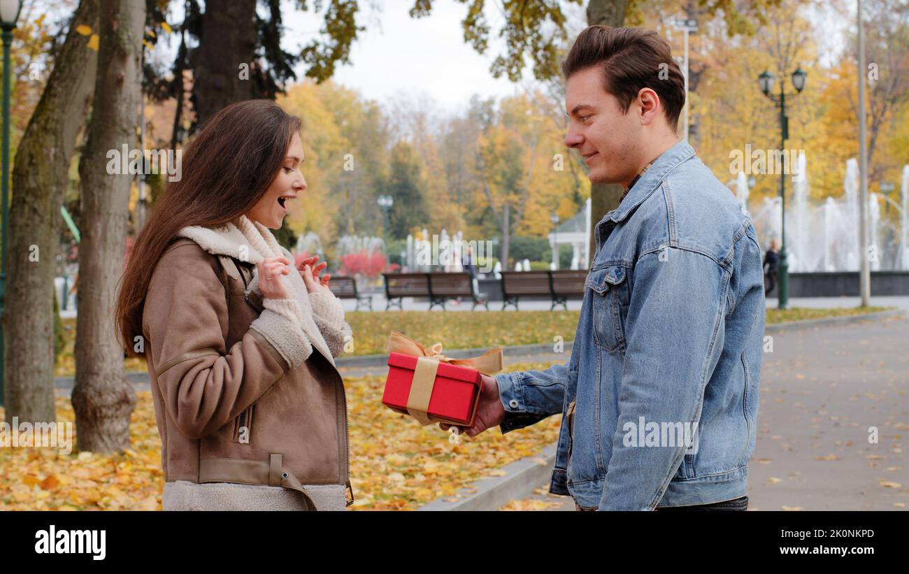 Caucasian boyfriend give red box small gift with gold ribbon to lovely pretty girlfriend young woman in autumn park surprise present for valentine's Stock Photo