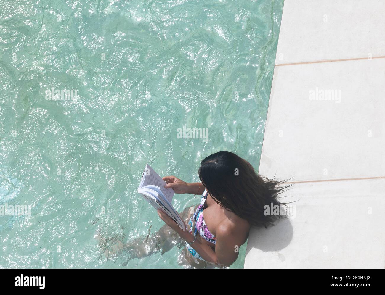 A young woman reading and relaxing surrounded by a luxury pool on vacation in the Caribbean, Mexico Stock Photo