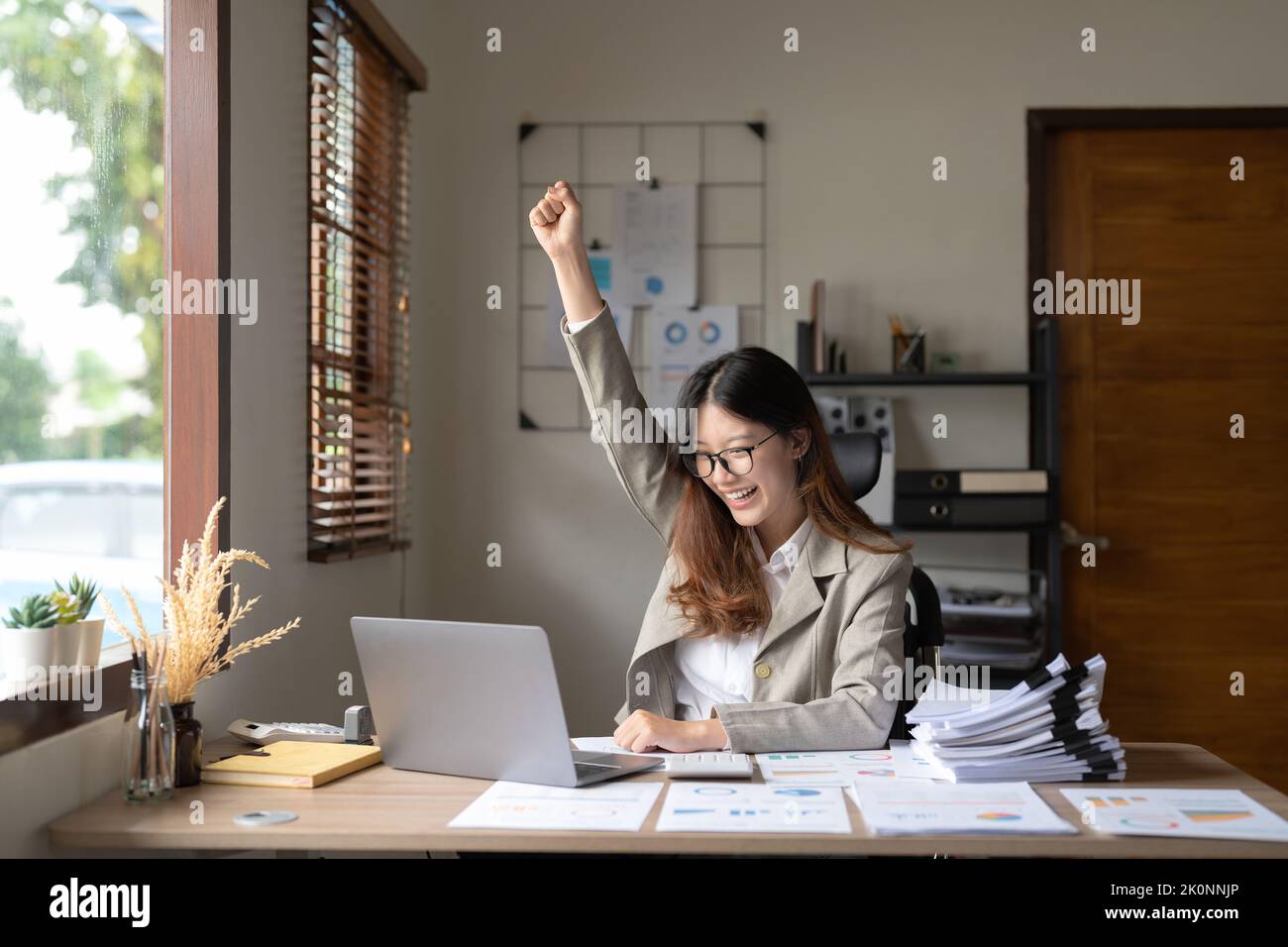 Successful young asian business woman achieving goals excited raised hands rejoicing with laptop on wokrplace in the office. Stock Photo