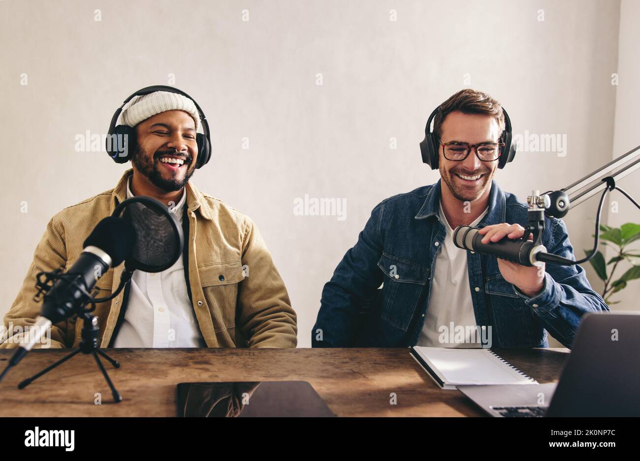 Male radio presenters having a great time on a live show. Two men smiling happily while recording an audio broadcast in a studio. College content crea Stock Photo