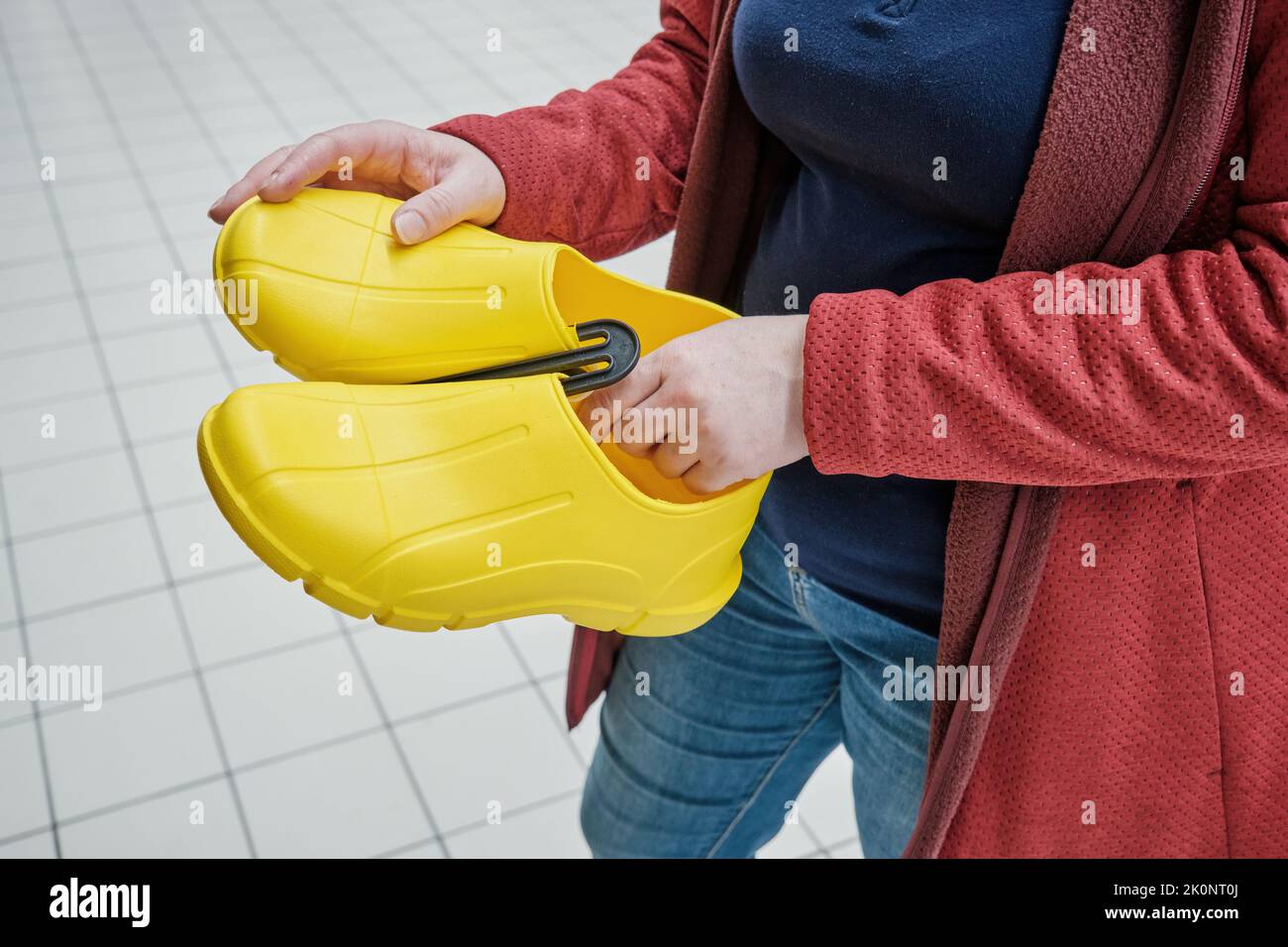 Pregnant woman in store chooses yellow rubber galoshes to buy. Hands close up Stock Photo