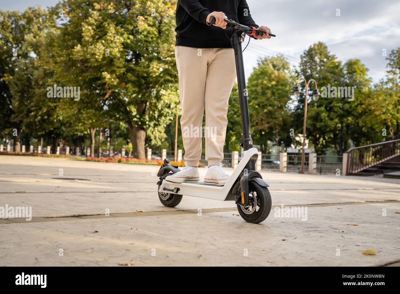 Feet of unknown man standing by or driving electric kick scooter e