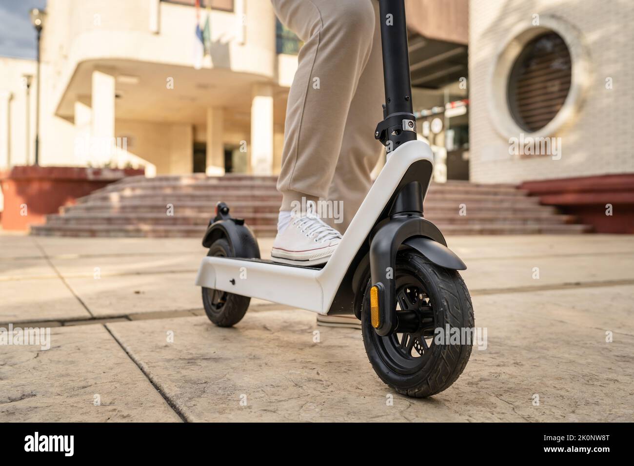 Feet of unknown man standing by or driving electric kick scooter e