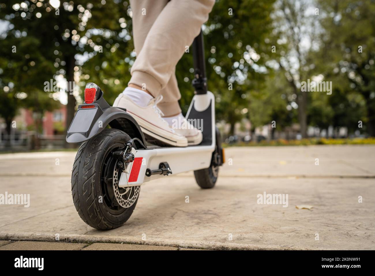 Feet of unknown man standing by or driving electric kick scooter e