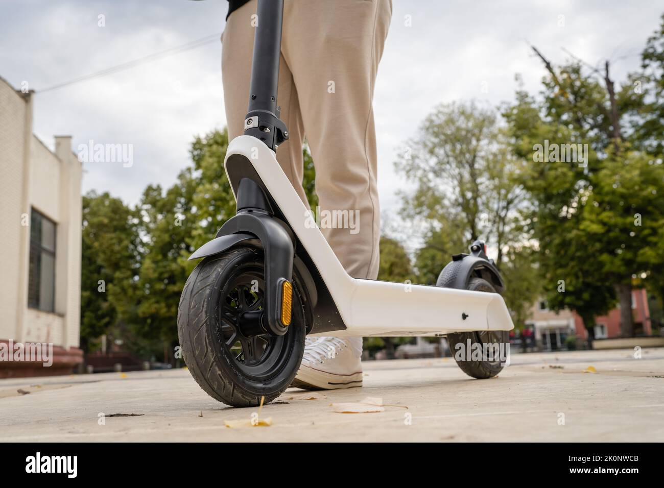 Feet of unknown man standing by or driving electric kick scooter e