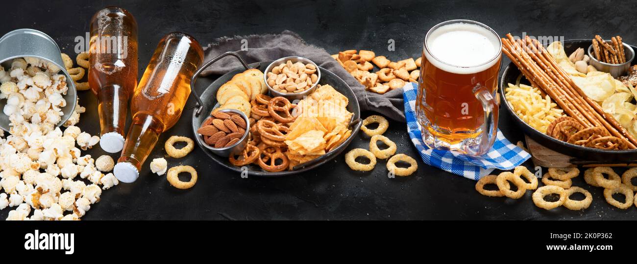 Assortment of beer and salty snacks on dark background. Party food concept. panorama Stock Photo