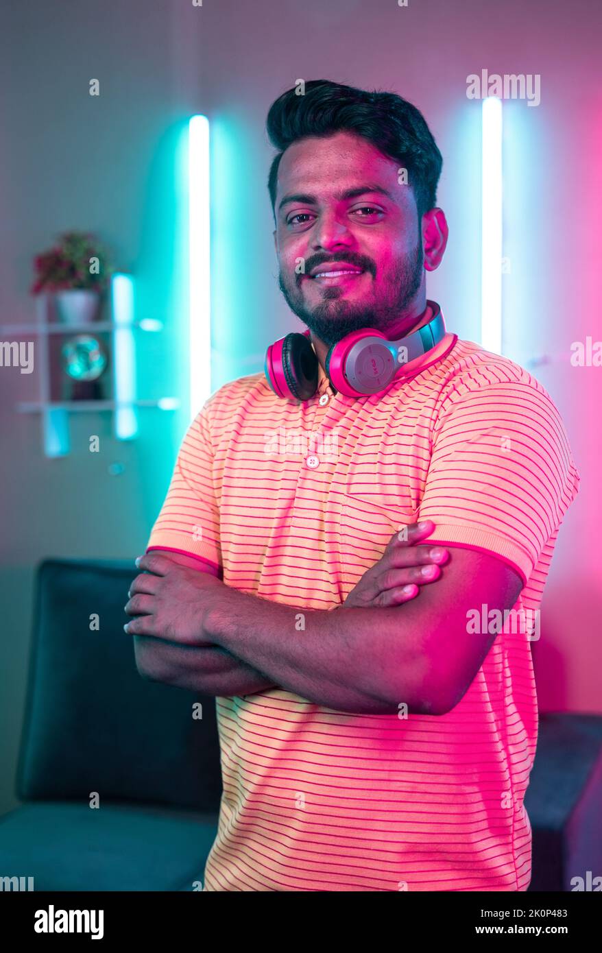 vertical shot of Happy smiling professional gamer standing with arms crossed by looking at camera on neon background - concept of social media Stock Photo
