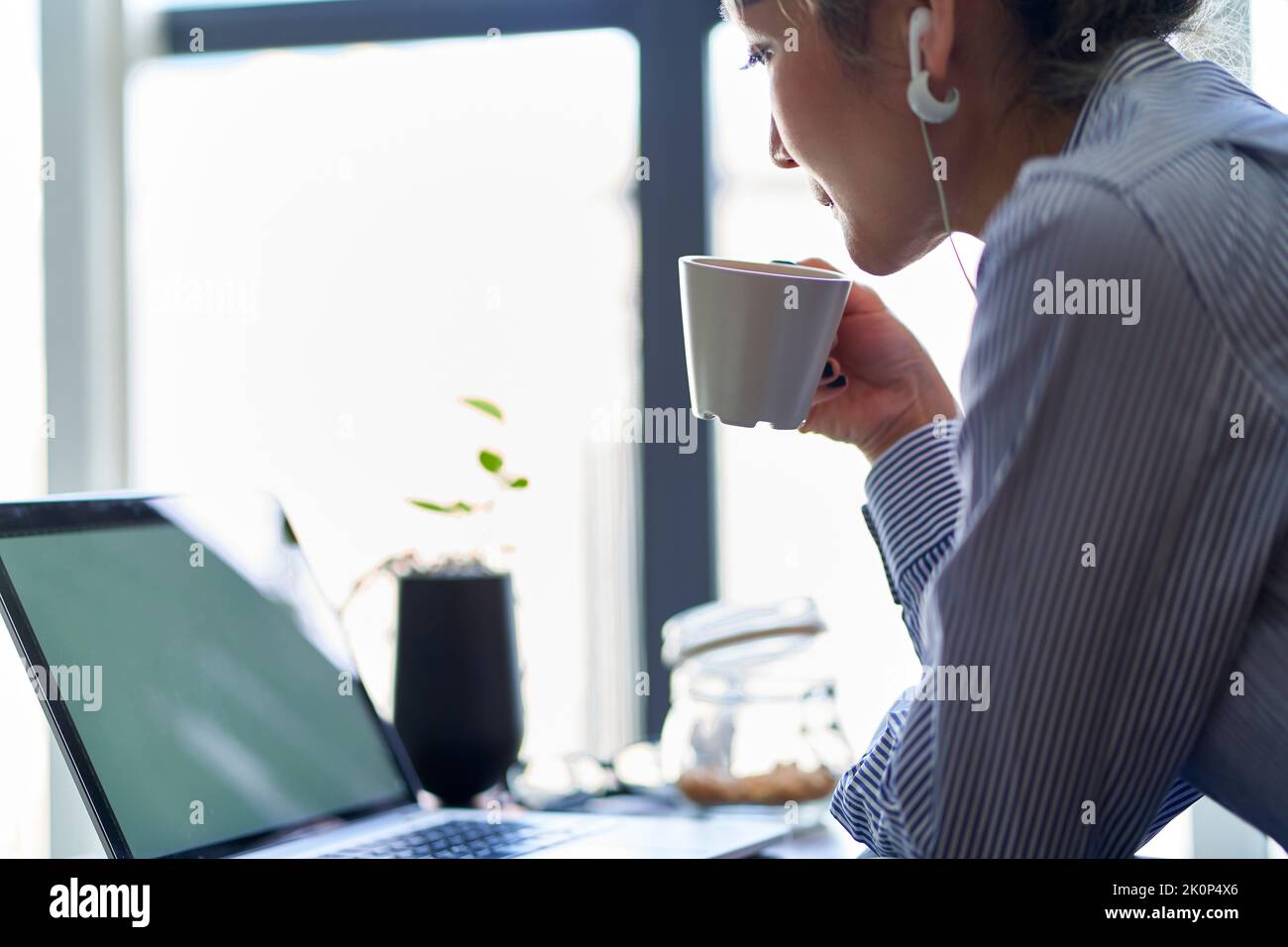 mature professional asian woman working from home sitting in couch drinking coffee while looking at laptop computer Stock Photo
