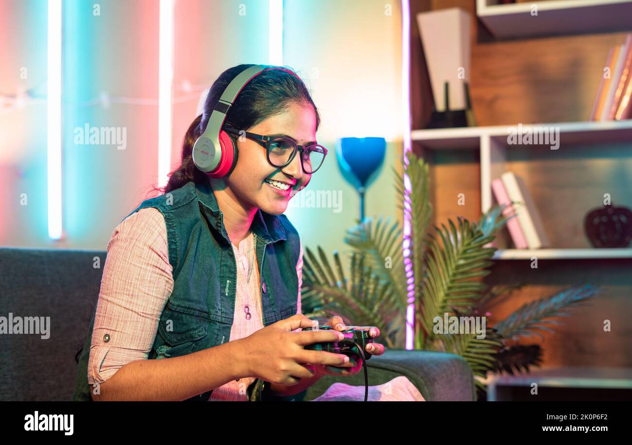 side view of happy girl playing video game using joystick on while sitting on sofa at home with copy space - concept of relaxation, hobby and Stock Photo