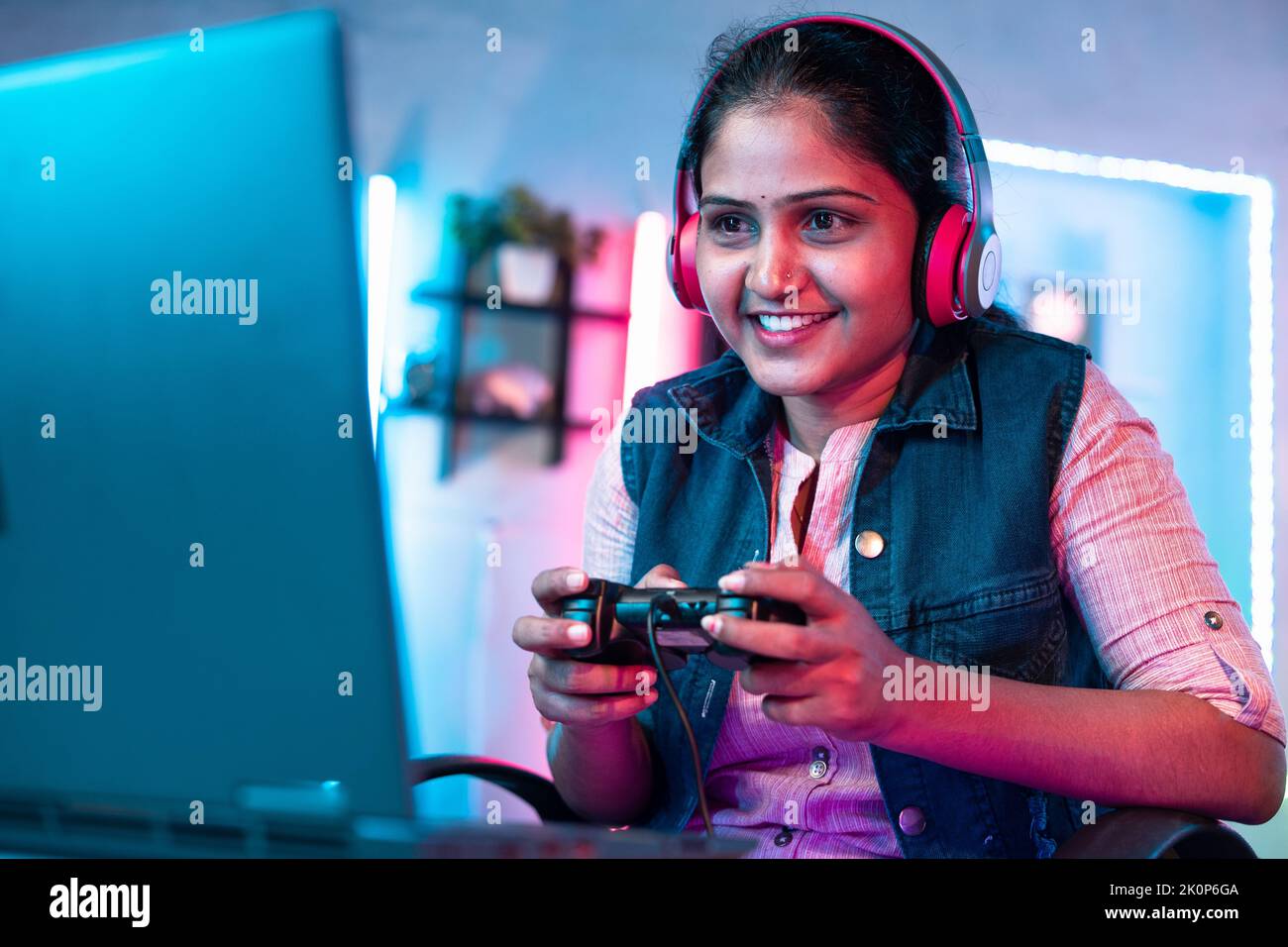 Confident girl with headset playing video game on laptop using joystick at home - concept of leisure activities, cyberspace and entertainment Stock Photo