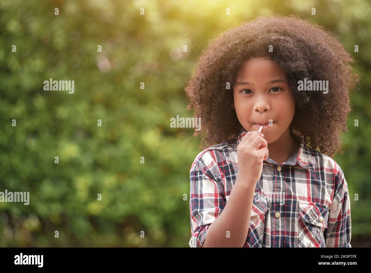 Happy African-American kid girl with a lollipop in her hands in the garden or outdoors. Stock Photo