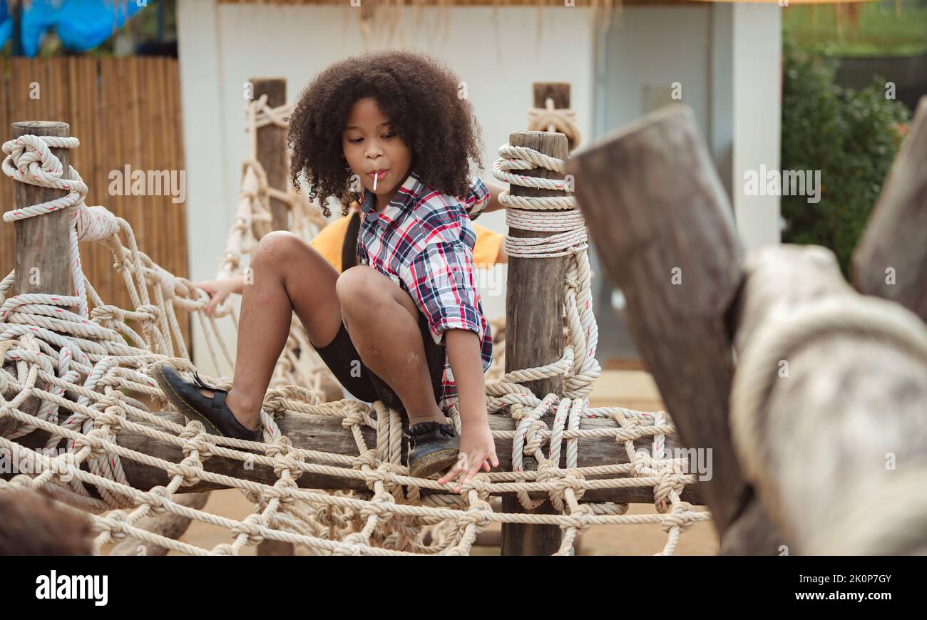 African american kid girl playing on a Rope-ladder web in a playground. Stock Photo