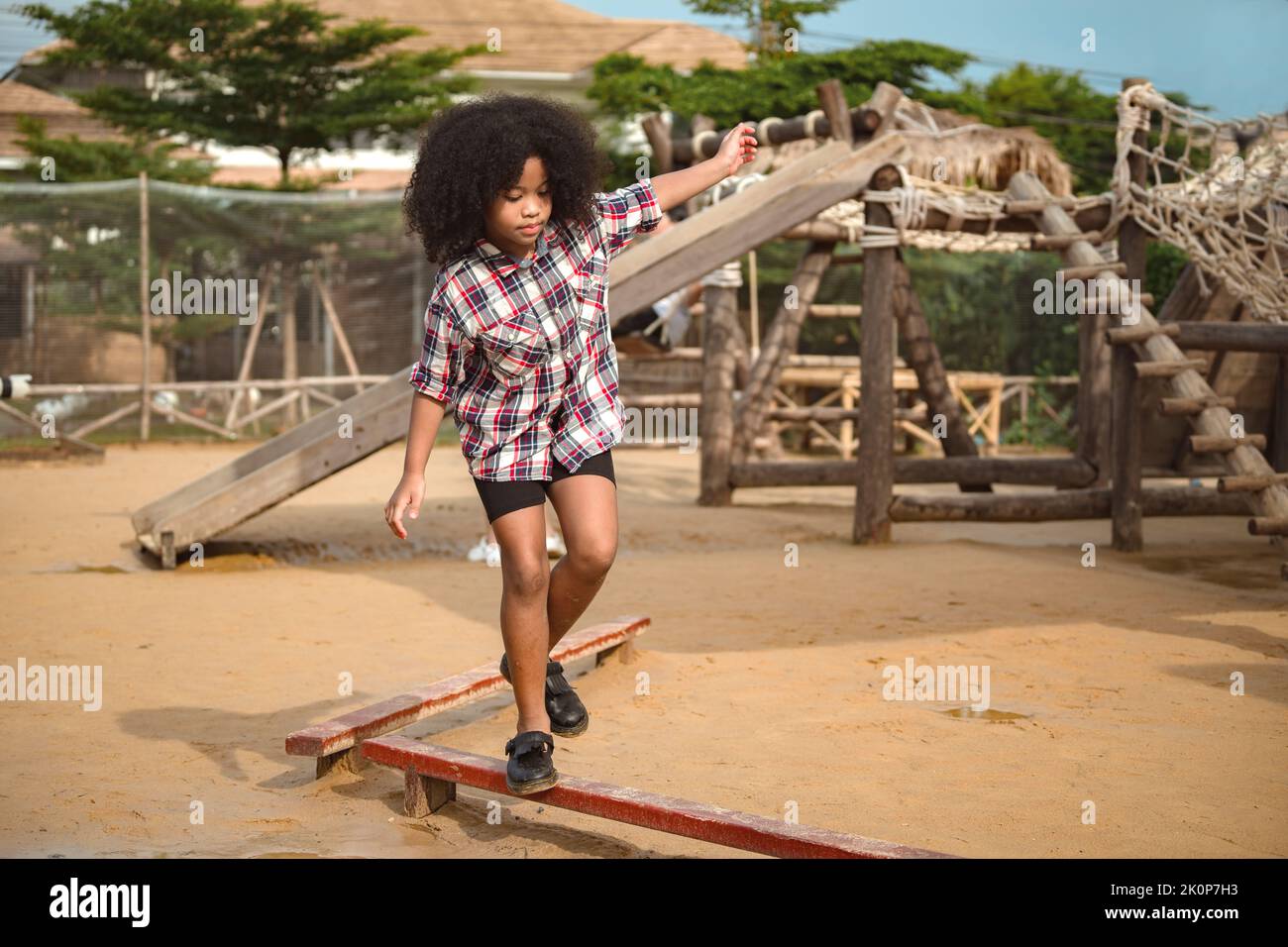 African-American girl kid walks on a log, keeping her balance, walking on the playground. Stock Photo
