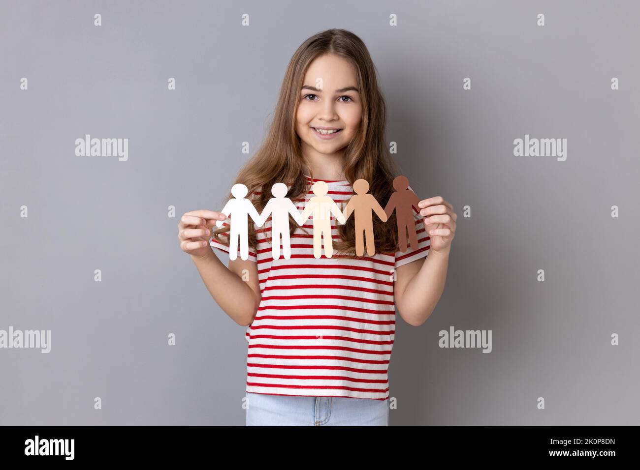 Portrait of little girl wearing striped T-shirt holding paper chain multiracial people, community, unity, people and support concept. Indoor studio shot isolated on gray background. Stock Photo