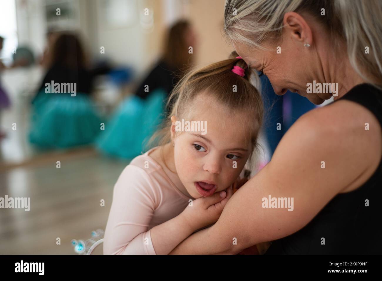 Little girl with down syndrome waiting for ballet class with her mother. Concept of integration disabled children and parenthood. Stock Photo