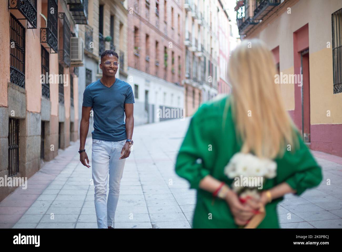 Selective focus on a african man walking towards a woman hiding a bouquet of flowers Stock Photo