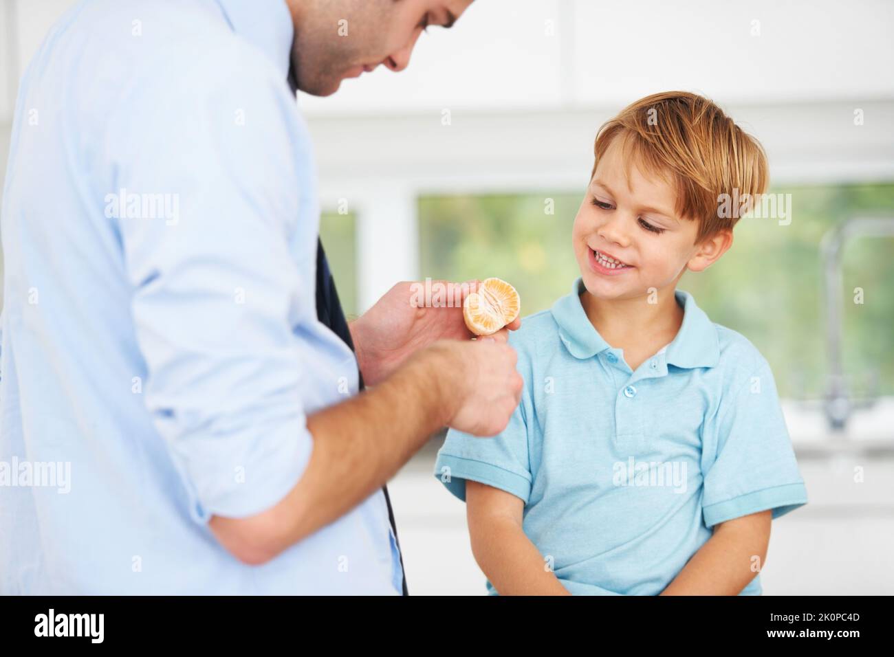 Heres your half...A young father giving half of an orange to his little boy. Stock Photo