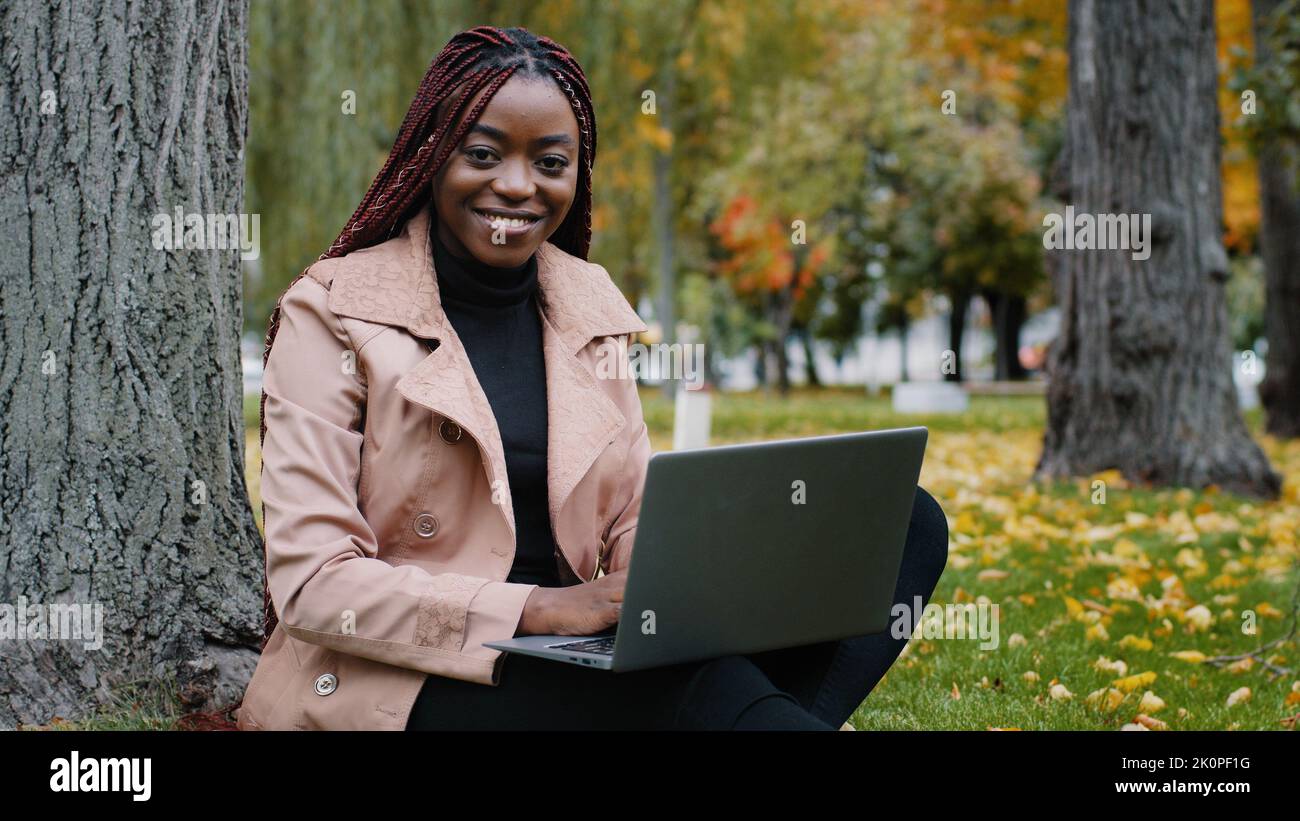 Focused young stylish african american woman freelancer writer journalist typing on laptop working in autumn park works remote using computer Stock Photo