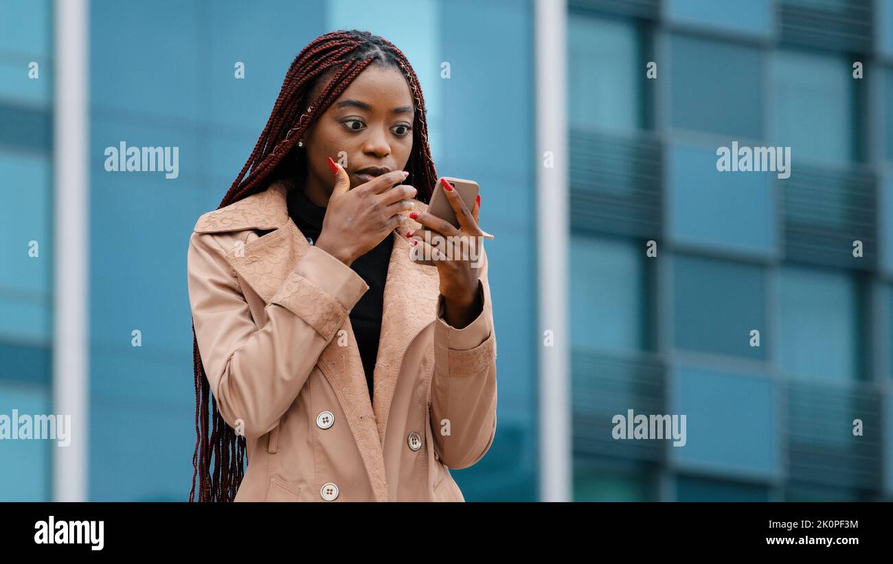 Upset shocked young woman standing outdoors receiving email on cellphone reading bad news sad distressed girl feels frustration after reads sms Stock Photo