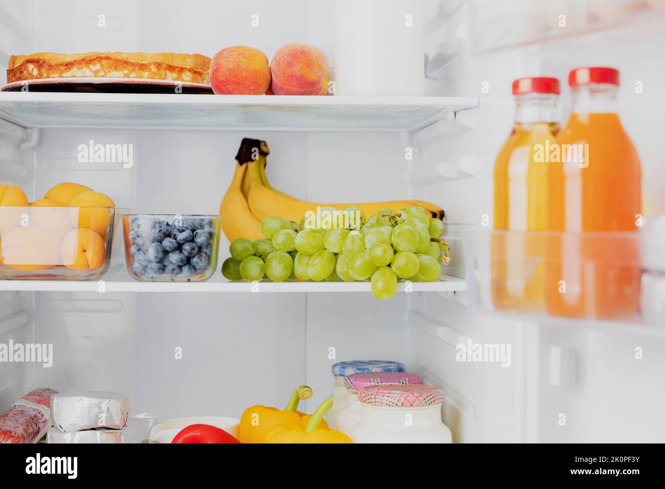 Front View of open two door fridge or refrigerator door filled with fresh fruits, vegetables, juice, full of healthy food items and ingredients inside. Electric Kitchen and Domestic Major Appliances Stock Photo
