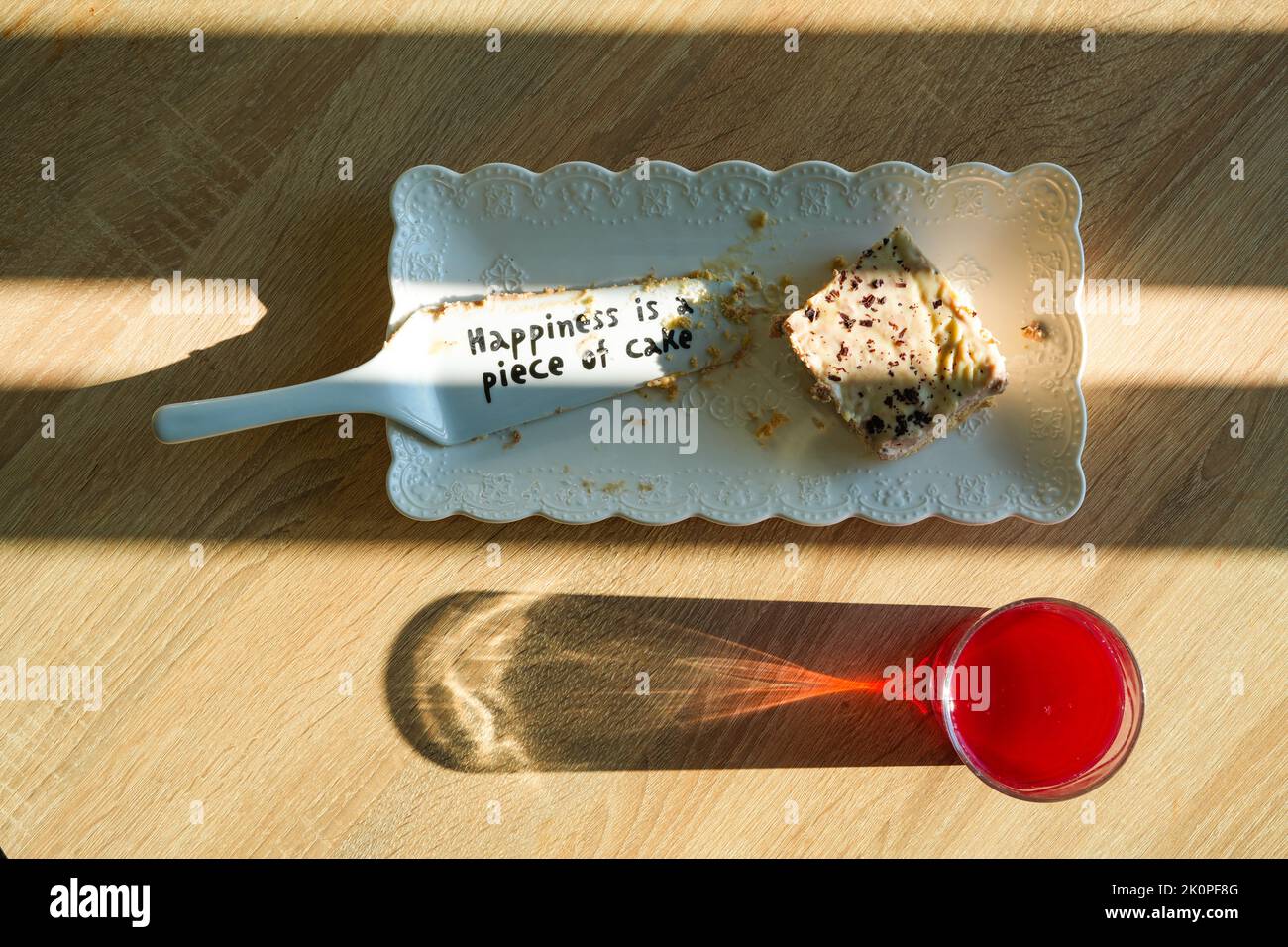 Cake sprinkled with chocolate chips in a plate with a cake scoop that says 'Happiness is a piece of cake' with juice in a glass on the table Stock Photo