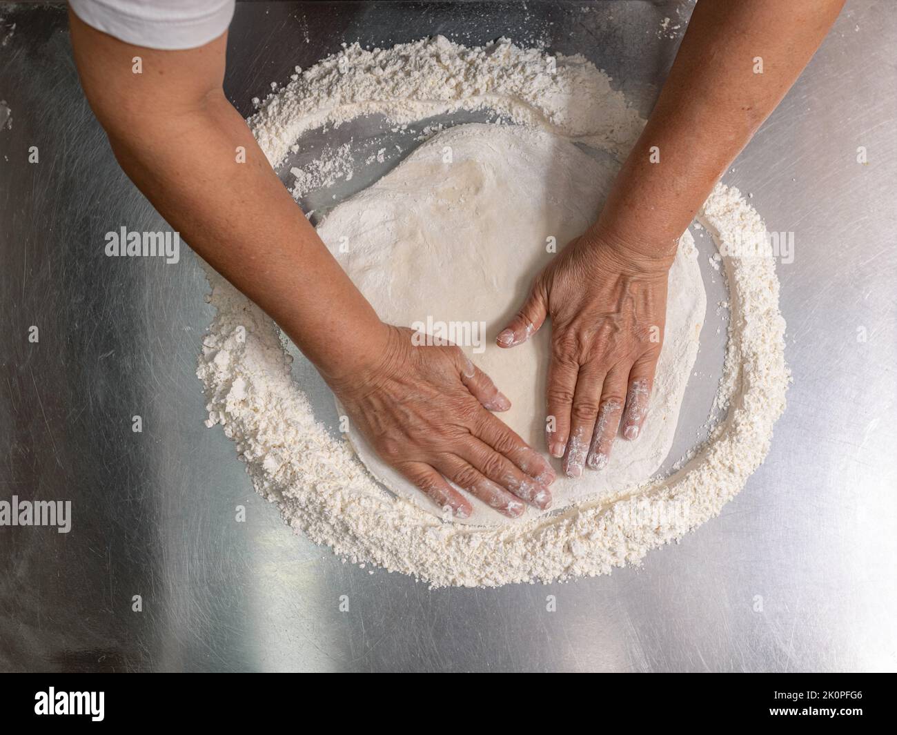 Woman making pizza dough on stainless steel counter Stock Photo