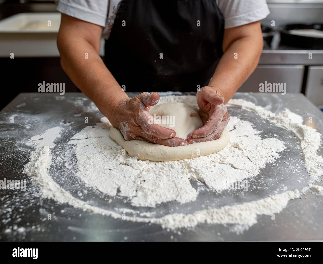 Woman making pizza dough on stainless steel counter Stock Photo