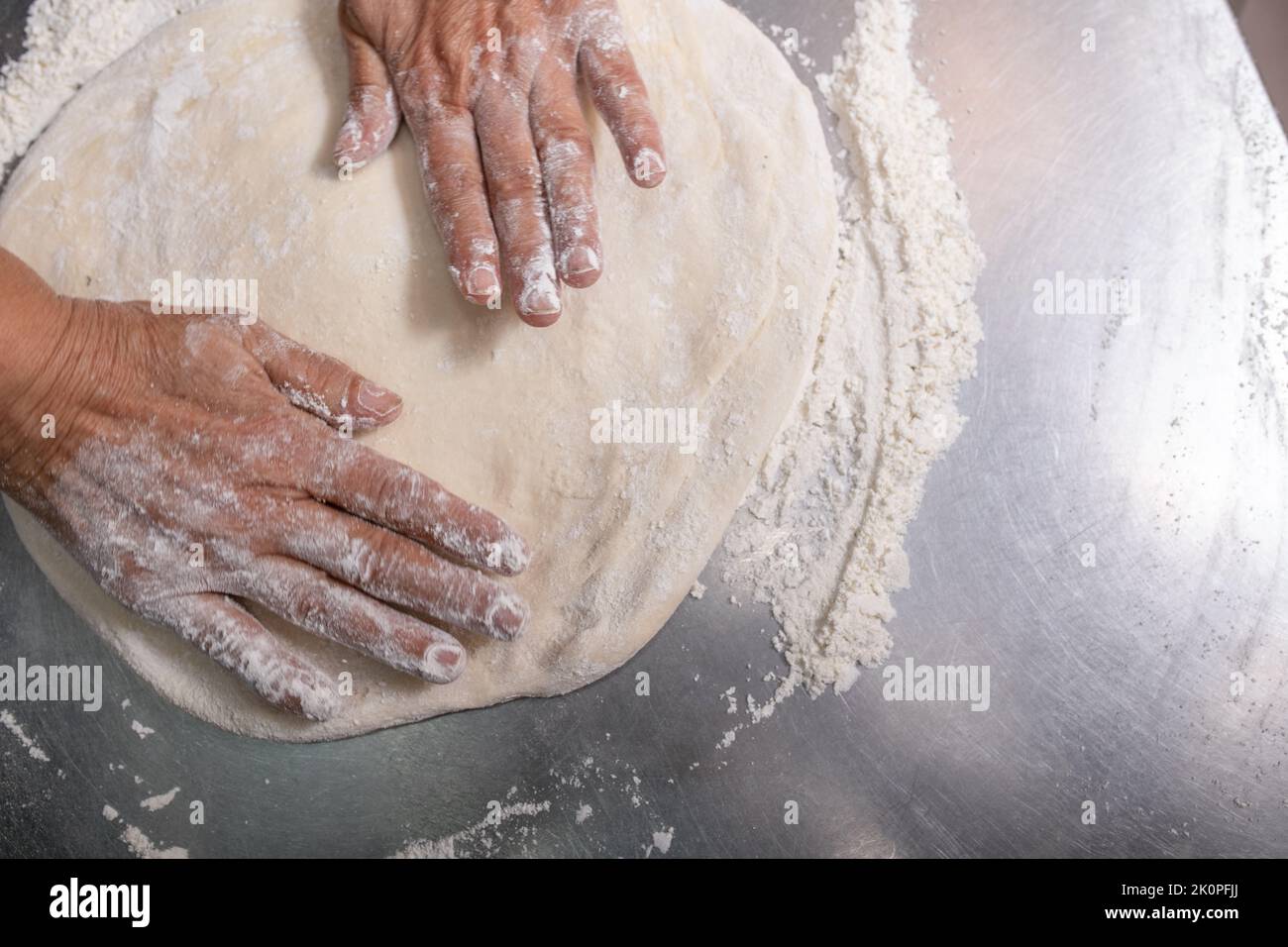Woman making pizza dough on stainless steel counter. Motion blur Stock Photo