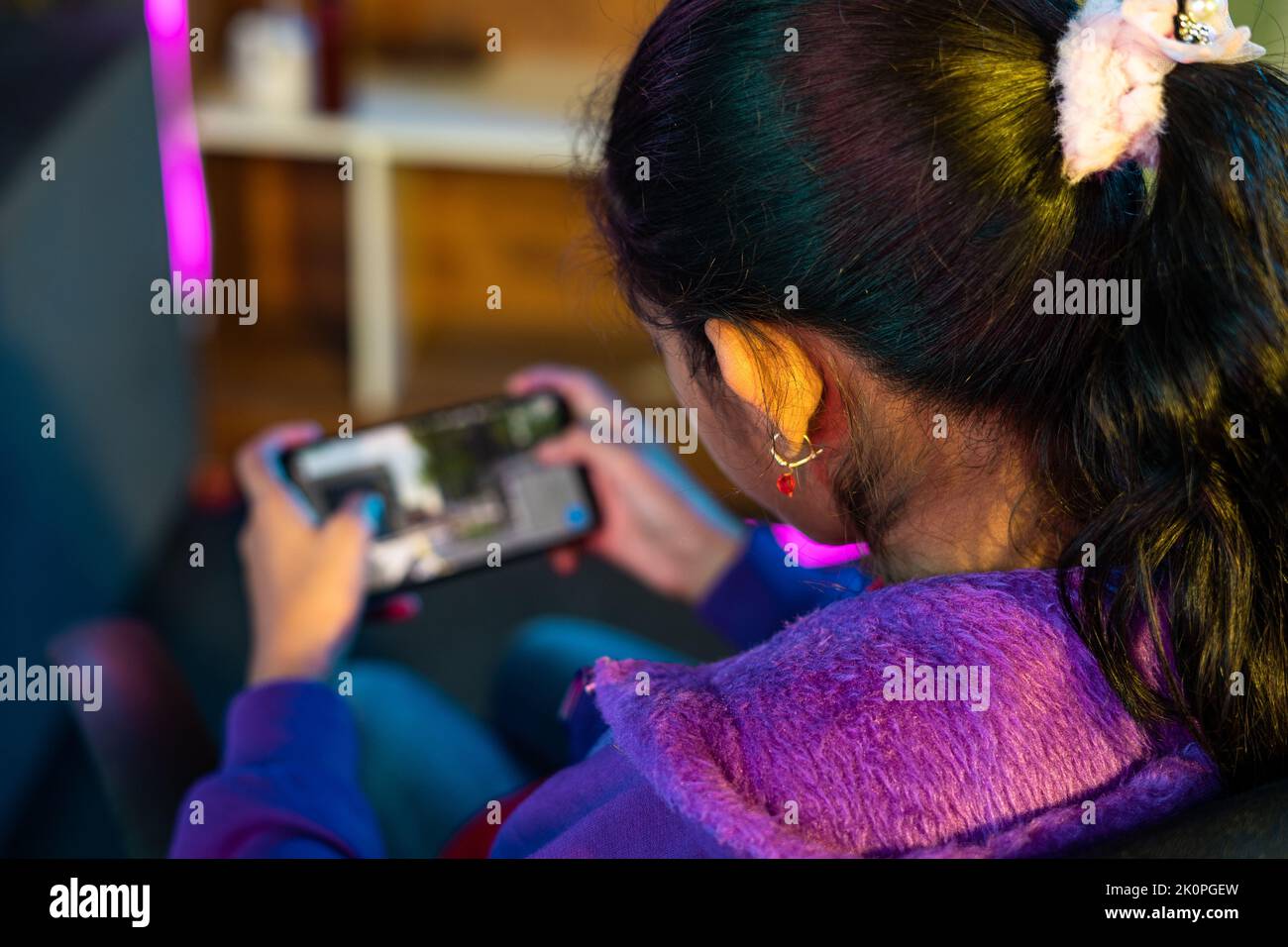 focus on girl, Shoulder shot of girl playing live video game on mobile phone at home - concept of relaxation, championship and tournament. Stock Photo