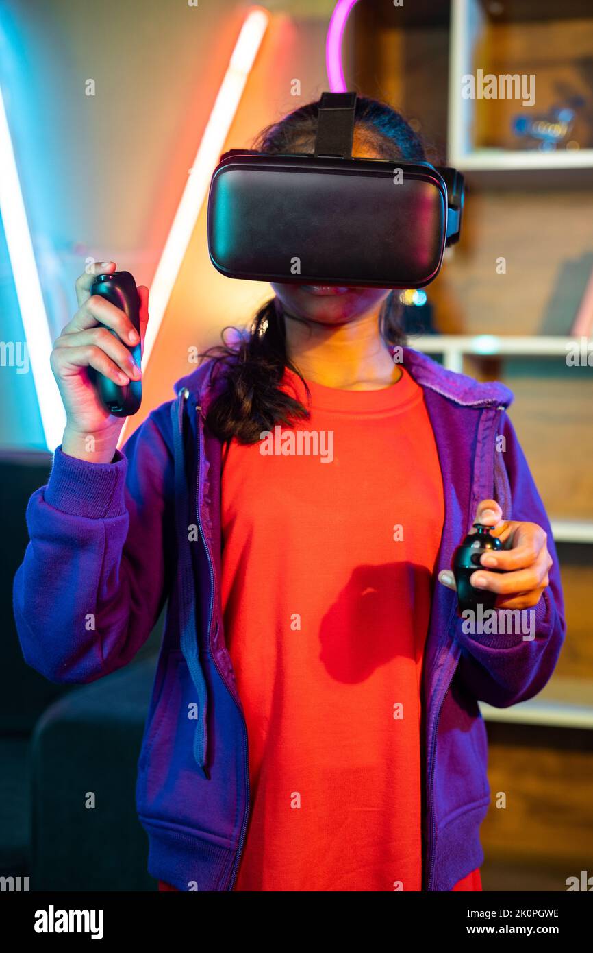 vertical shot of Young teenager girl playing video game on virtural reality or VR headset using joystick at home on neon background - concept of Stock Photo