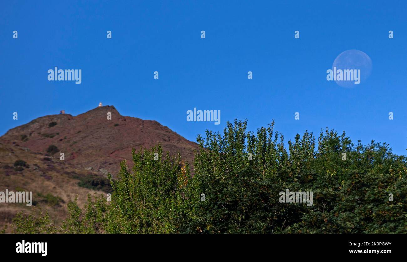 Holyrood Park Edinburgh, Scotland, UK 13th September 2022. Waning Gibbous Moon 90% appearing in the morning sky to the right of Arthur's Seat summit  with a backdrop of blue sky. Temperature 13 degrees centigrade. Credit/Arch White/alamy live news Stock Photo