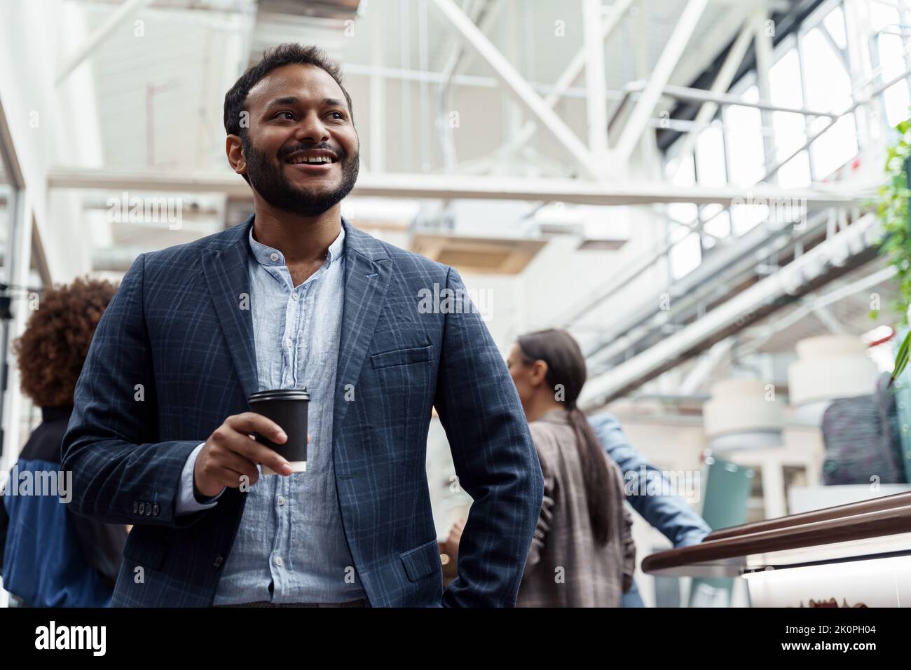 Smiling indian businessman drinking coffee and looking side while standing in office Stock Photo