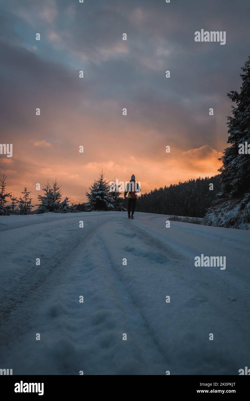 Candid portrait of a man in winter clothes standing at the end of a path watching the sunrise in the snowy area of Stare Hamry Beskydy mountains, Czec Stock Photo