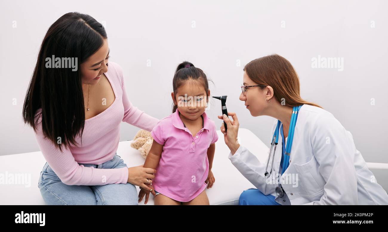 Korean child with her mother during hearing test, audiologist with otoscope checking ear of asian little girl. Hearing exam Stock Photo