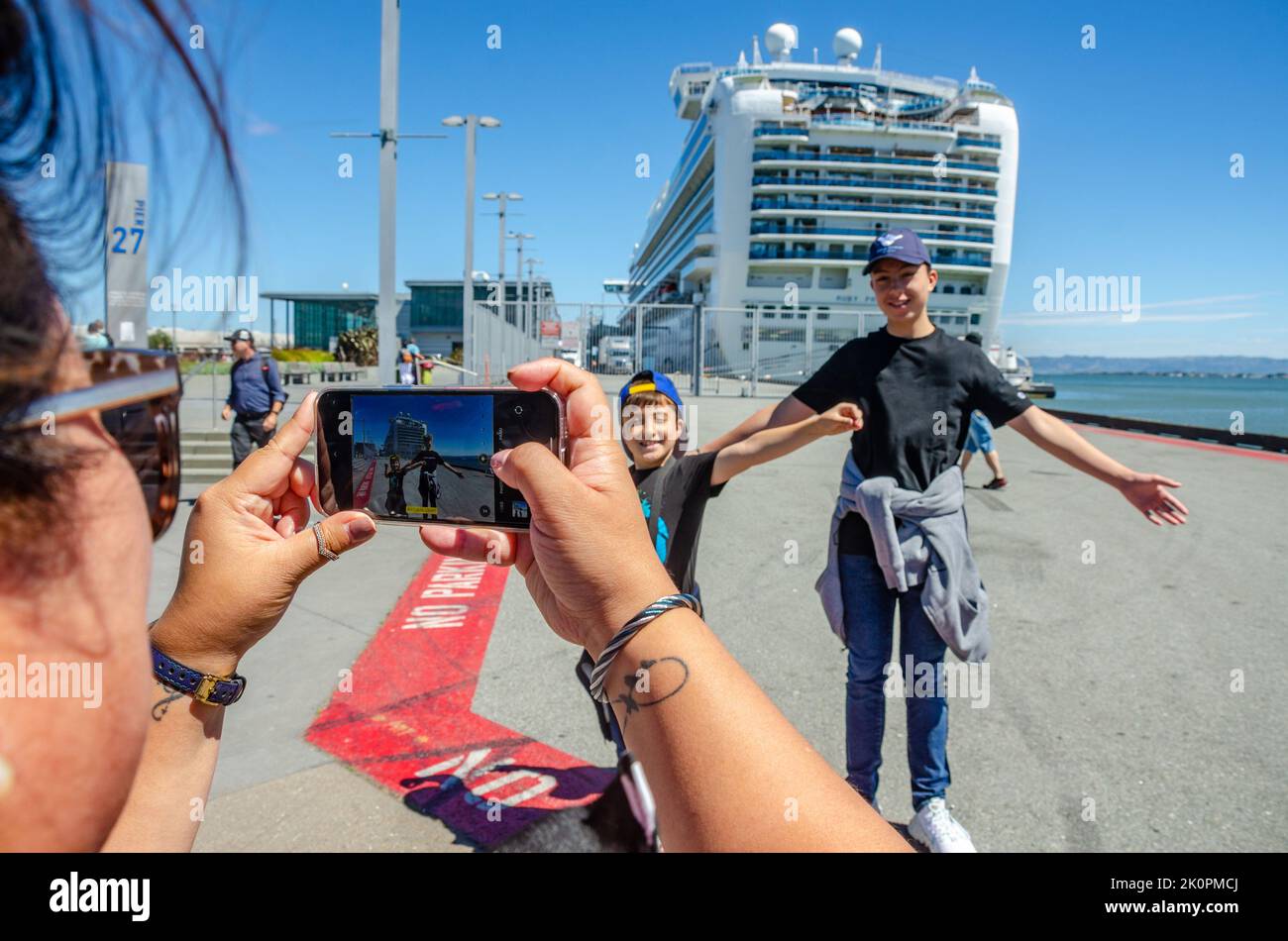 A lady takes a photo of family in front of Ruby Princess, a cruise liner docked at The James R Herman Cruise Terminal at Pier 27 in San Francisco Stock Photo