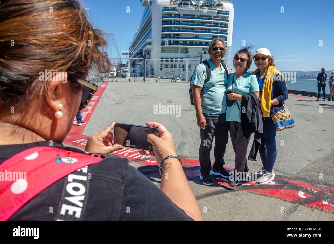 A lady takes a photo of family in front of Ruby Princess, a cruise liner docked at The James R Herman Cruise Terminal at Pier 27 in San Francisco Stock Photo