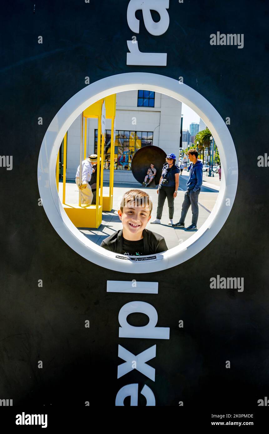 Portrait of a boy peering through the circular hole in an Exploratorium sign in San Francisco, California Stock Photo