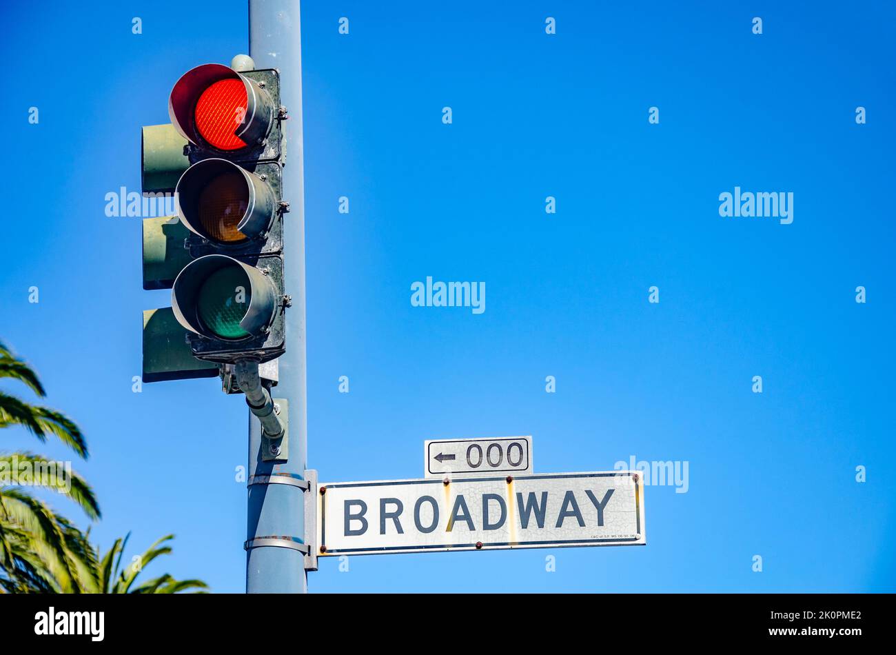 A red traffic light and a street sign for 'Broadway' against a clear blue summer sky in San Francisco, California Stock Photo