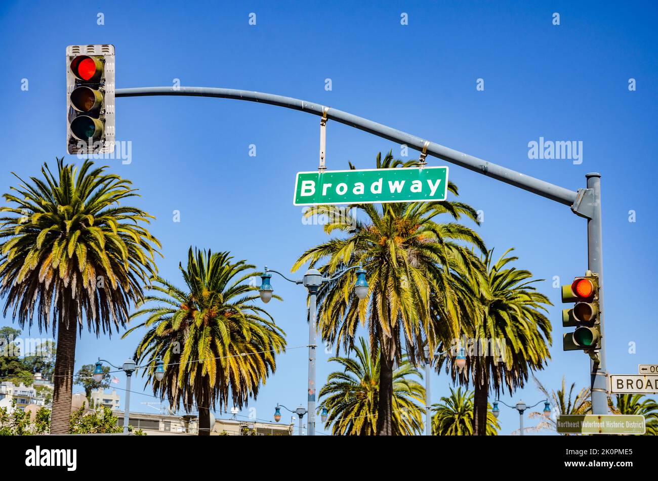A street sign for Broadway hanging from the crossbar of a traffic light in San Francisco pictured with palm trees and blue sky int he background Stock Photo